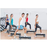 Group fitness class using aerobic step platforms at Aura Fit gym, gym equipment visible in background.