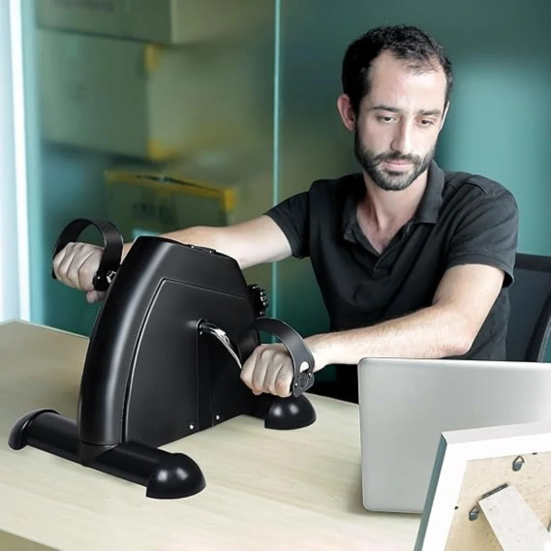 Man using a portable arm pedal exerciser at desk, fitness equipment by Aura Fit Pakistan
